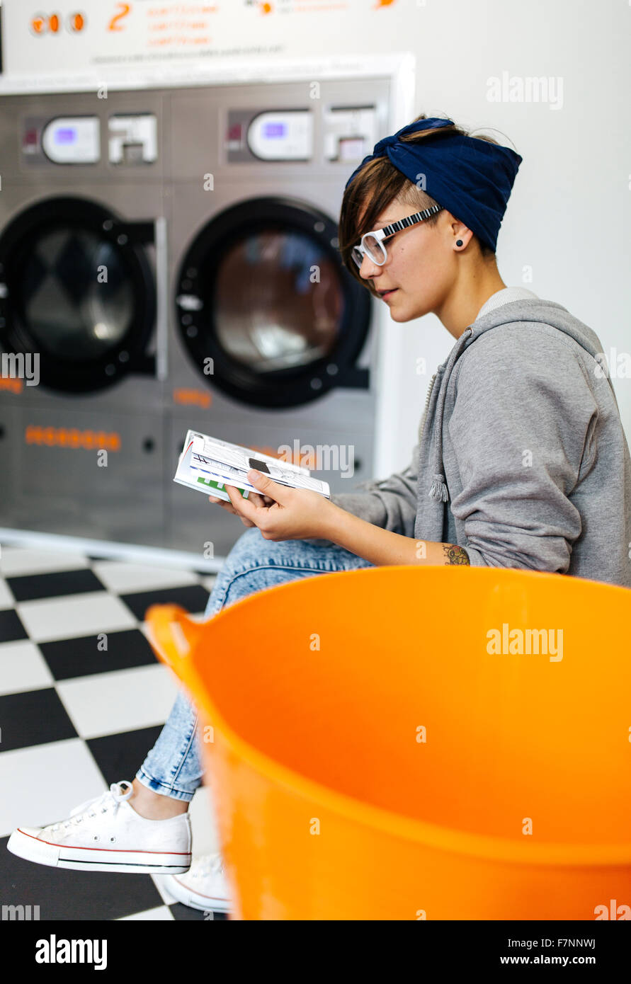 Young woman reading comic strip in a launderette Stock Photo