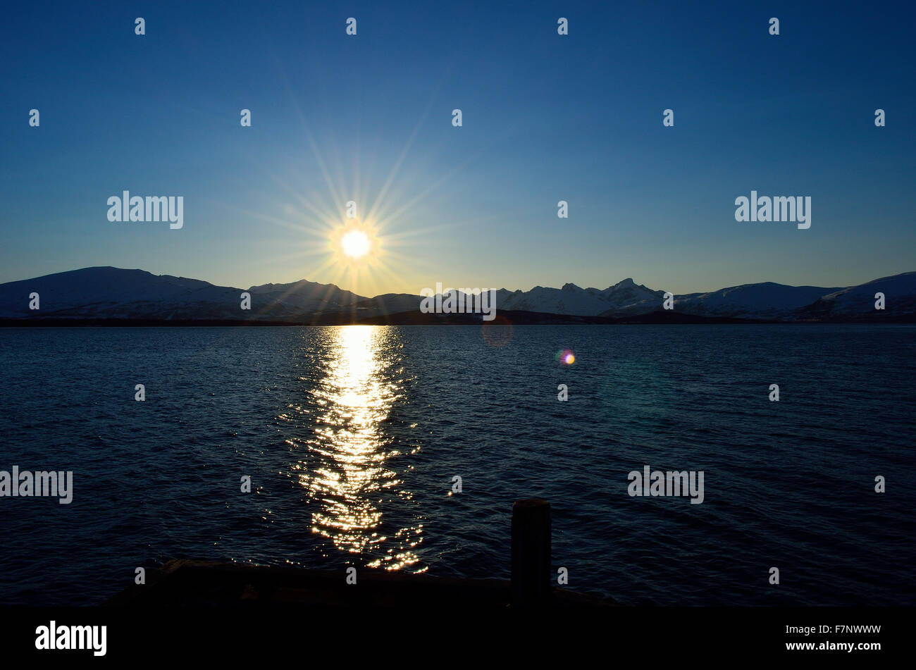 sunshine over blue fjord and pier with snowy mountain background Stock ...