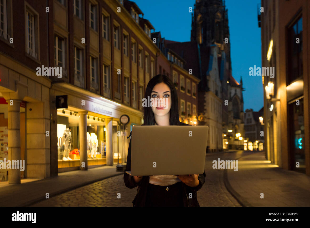 Germany, Muenster, portrait of young woman with laptop in the city at evening Stock Photo