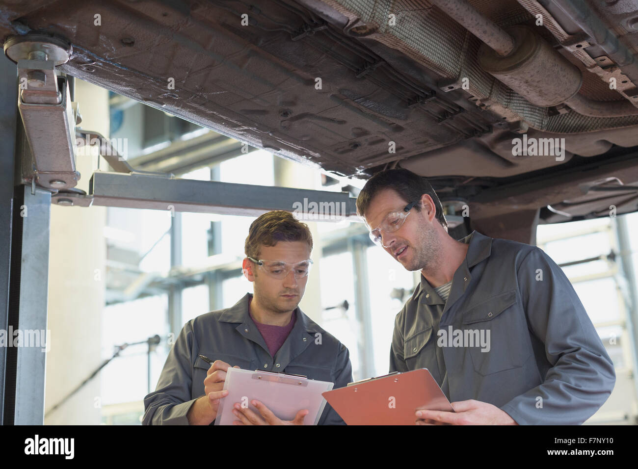Mechanics with clipboards talking under car in auto repair shop Stock Photo