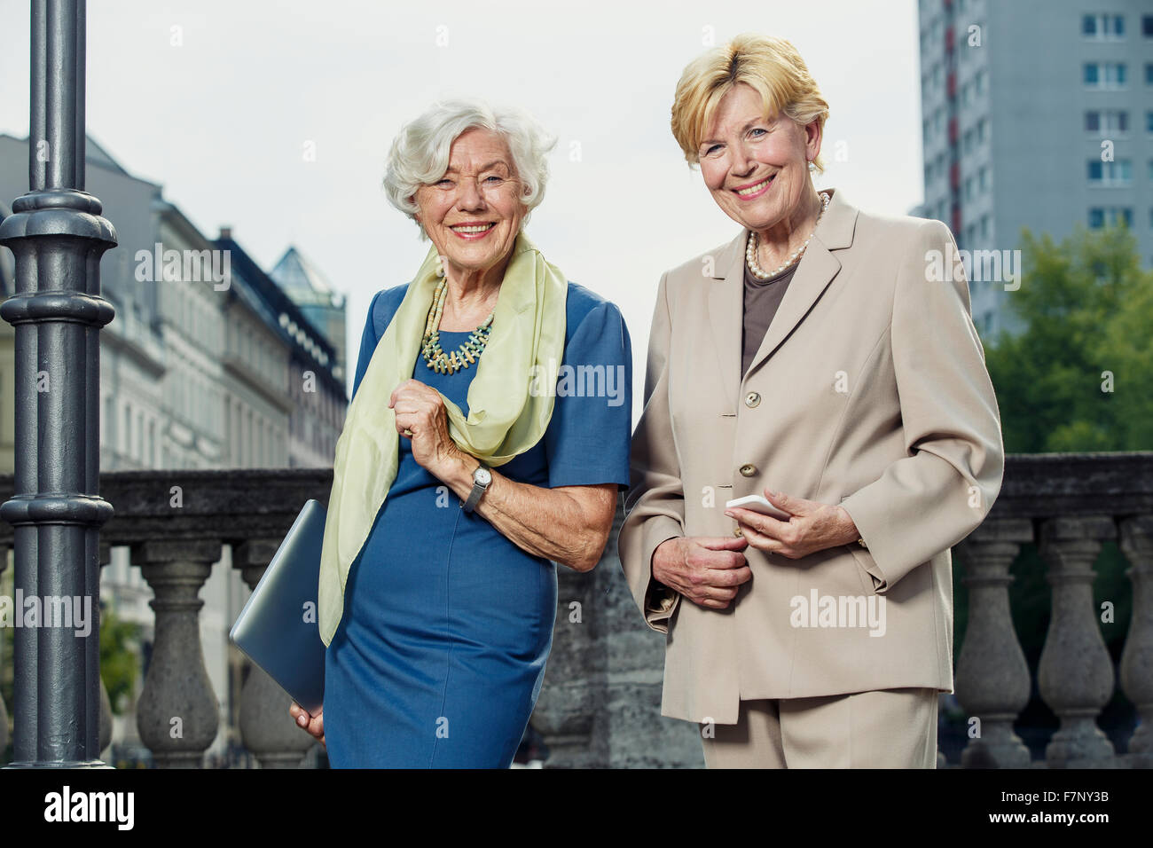 Germany, Berlin, portrait of two smiling senior businesswomen with laptop and smartphone Stock Photo