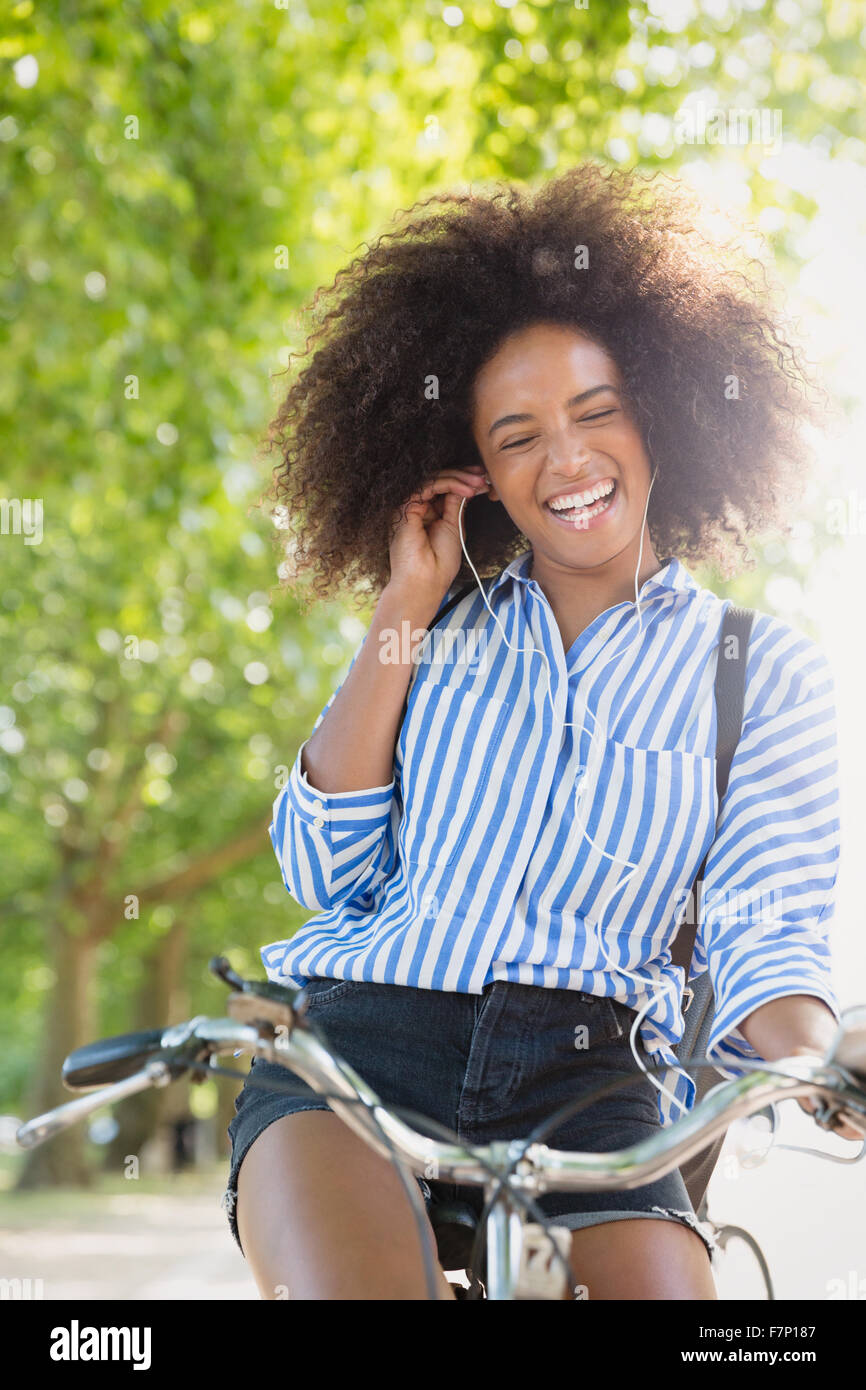 Enthusiastic woman with afro riding bicycle listening to music on headphones Stock Photo