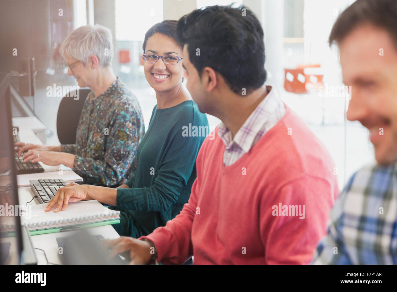 Smiling students talking at computers in adult education classroom Stock Photo