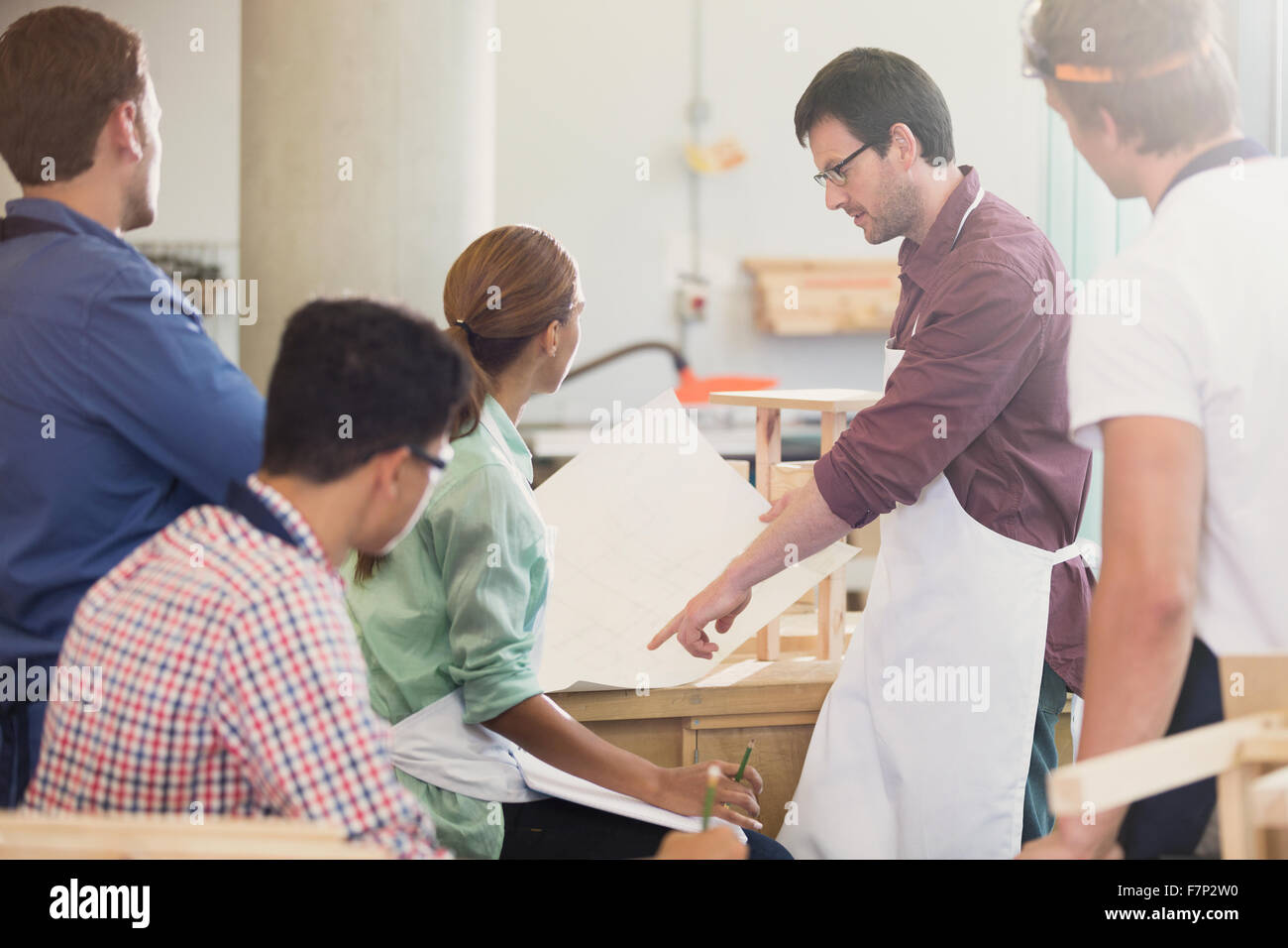 Carpentry teacher explaining blueprints to students in workshop Stock Photo