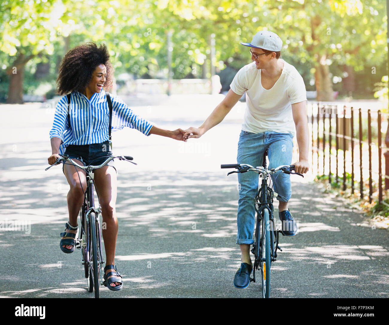 Couple holding hands riding bicycles in urban park Stock Photo