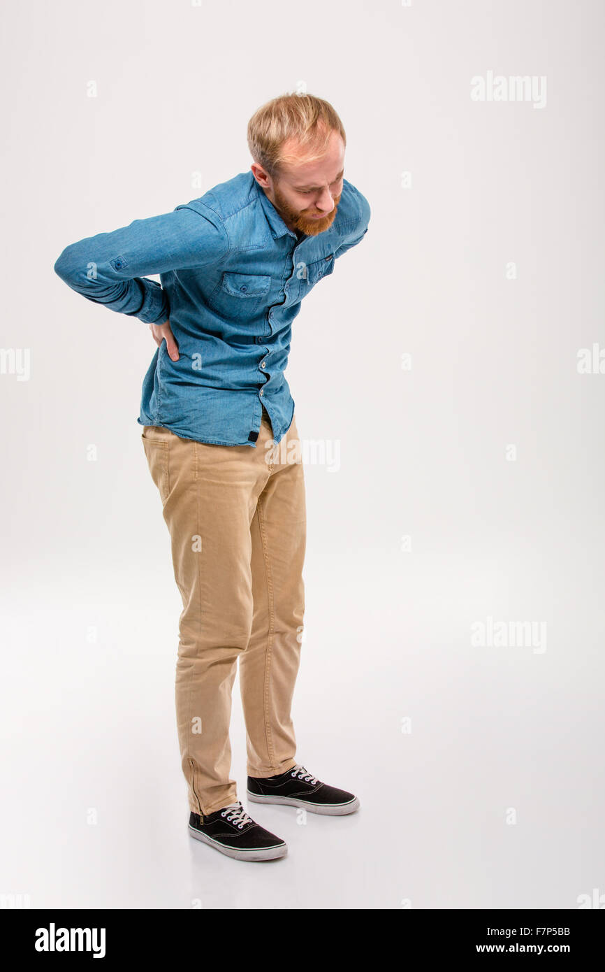 Full length portrait of young bearded man in jeans shirt and beige pants  having a back pain isolated over white background Stock Photo - Alamy