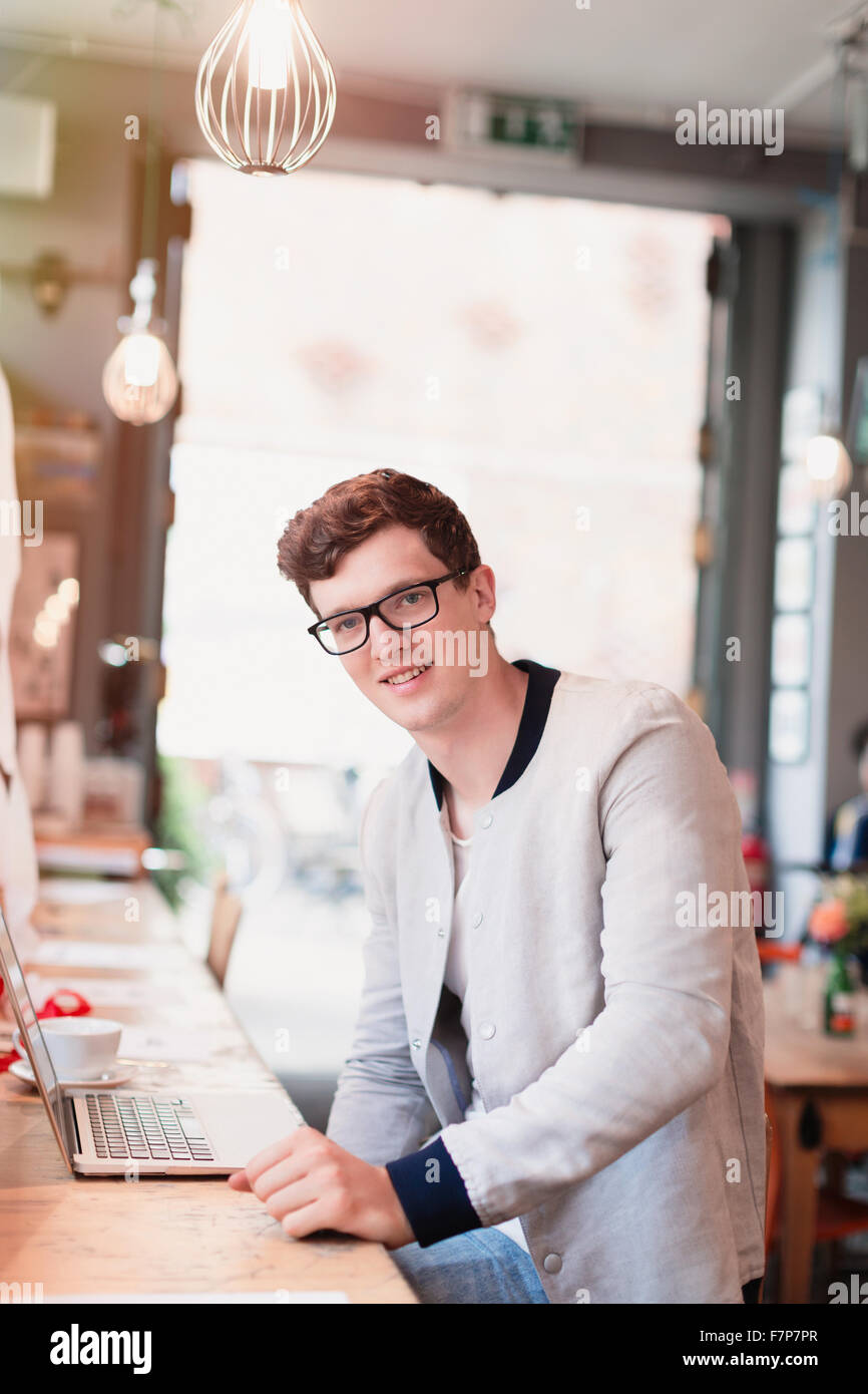 Portrait smiling man with eyeglasses using laptop in cafe Stock Photo