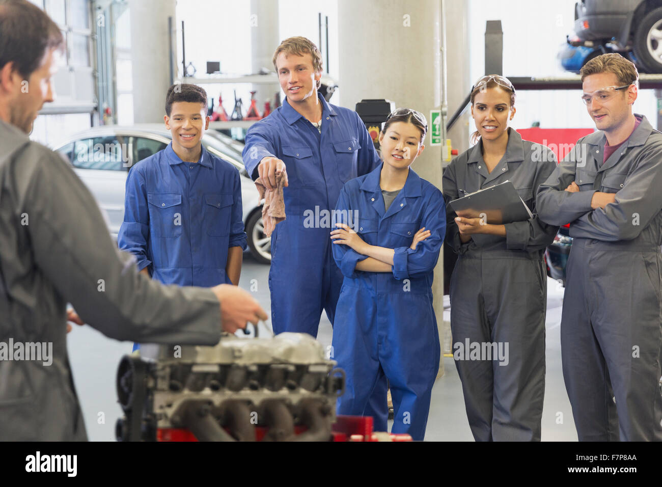 Mechanic and students discussing car engine in auto repair shop Stock Photo