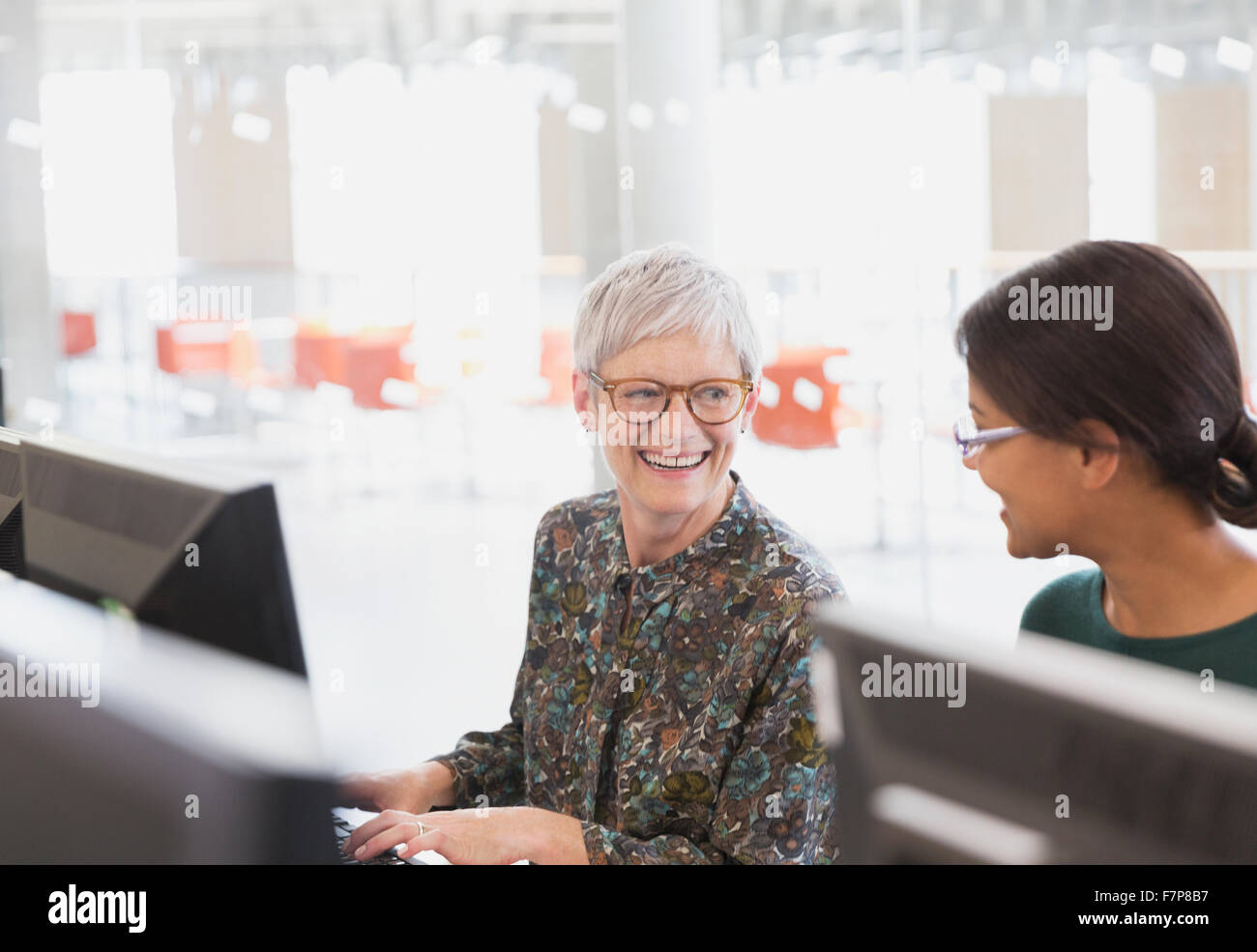 Smiling women talking at computers in adult education classroom Stock Photo