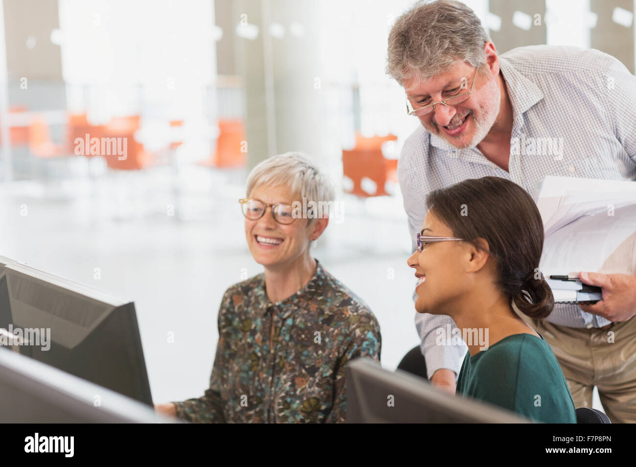 Smiling students talking at computer in adult education classroom Stock Photo