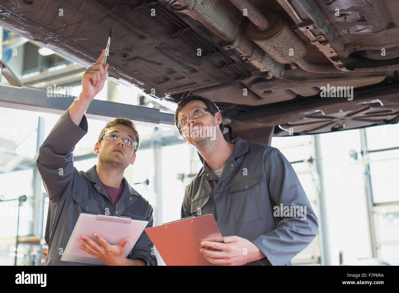 Mechanics with clipboards working under car in auto repair shop Stock Photo