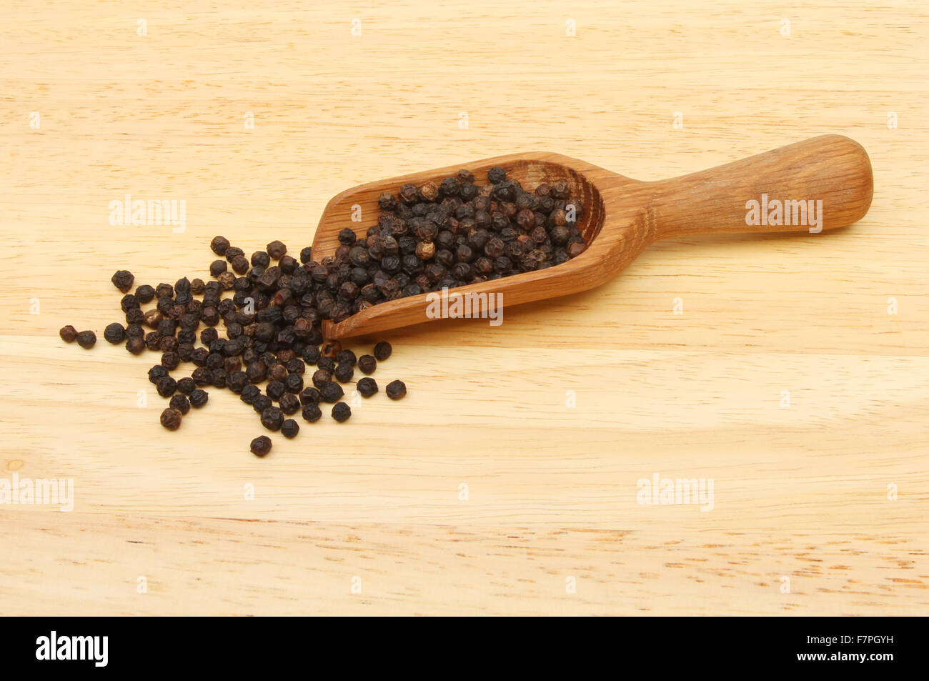Black peppercorns in a wooden scoop on a board Stock Photo