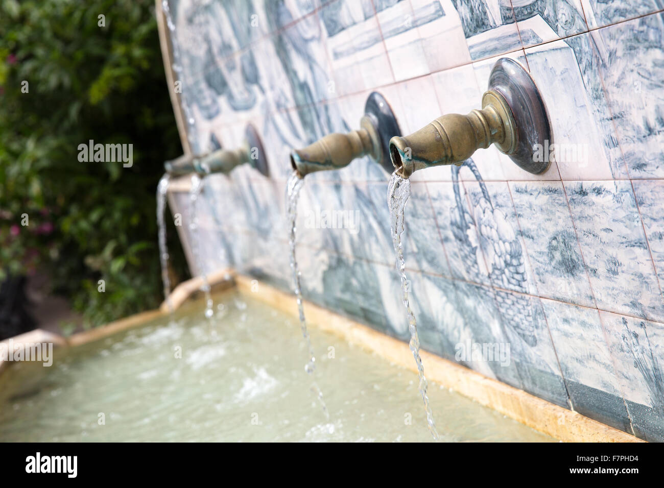 Streams of water coming out of some metal pipes in a village fountain with handmade ceramic drawings Stock Photo