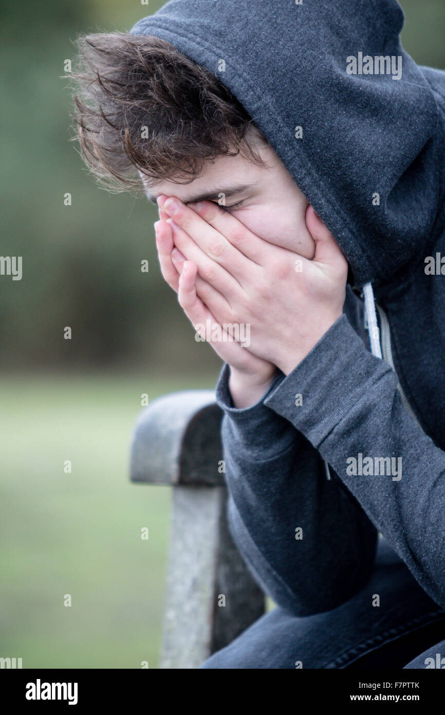 Sad teenage boy sitting on a park bench Stock Photo