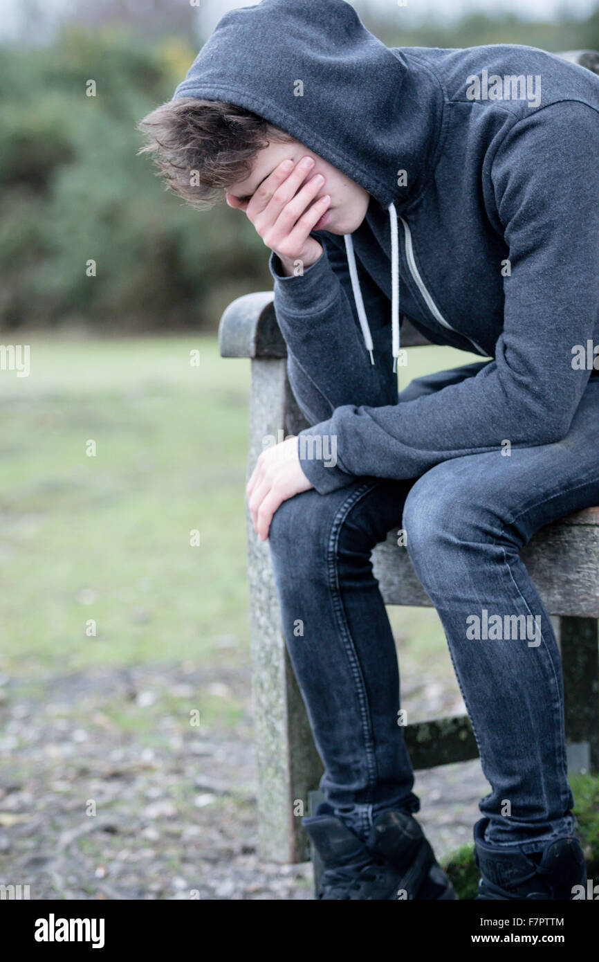 Sad teenage boy sitting on a park bench Stock Photo