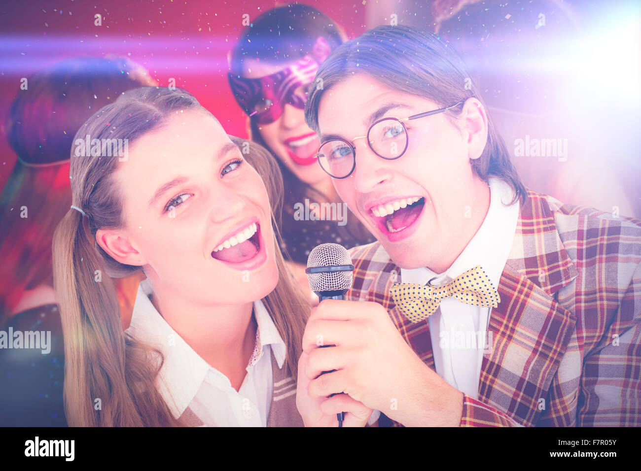 Composite image of happy geeky hipsters singing with microphone Stock Photo