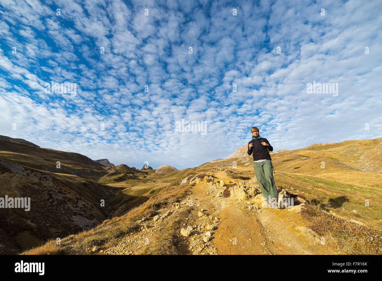 Female hiker walking on footpath in a colorful valley with scenic sky and clouds. Wide angle shot from below in the Italian Fren Stock Photo