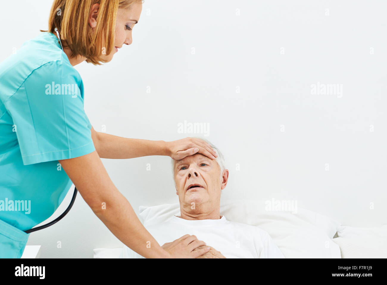 Old man with fever in bed with nurse touching his forehead Stock Photo