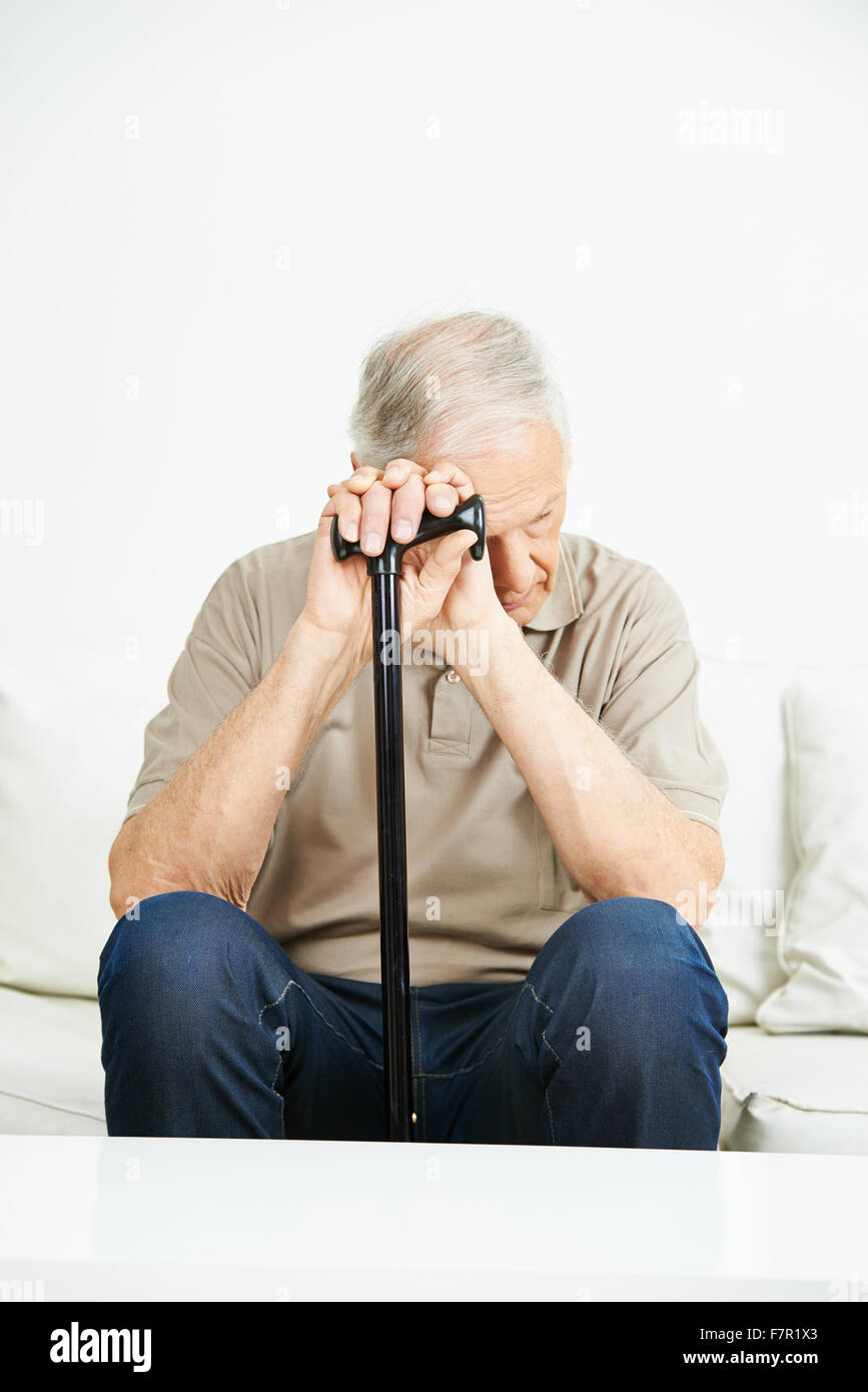 Sad senior man with cane sitting on a sofa Stock Photo