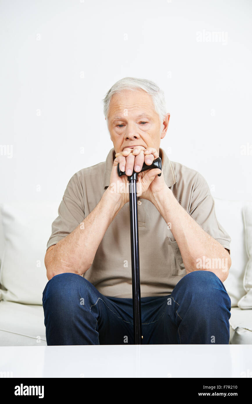 Sad old man with cane sitting pensive on a sofa Stock Photo