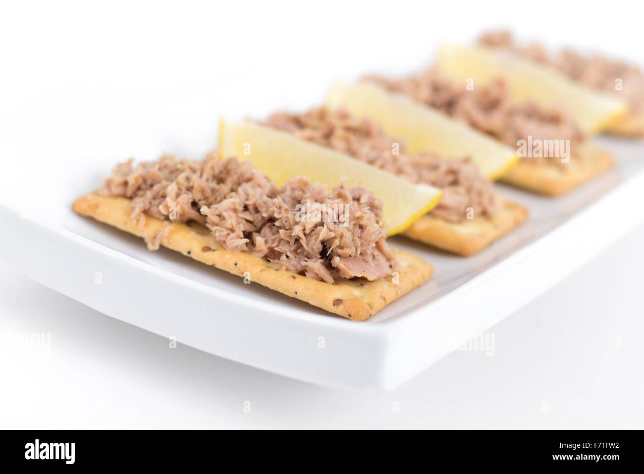 Tuna meat on crackers as snack or appetizer over white background Stock