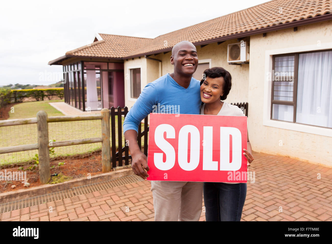 happy African couple standing outside their house and holding sold sign ...