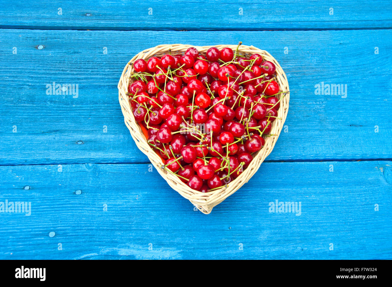 Heart shaped wicker basket full of cherries on blue old garden table wooden background Stock Photo