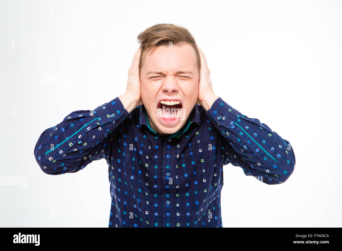 Hysterical mad young man in plaid shirt  closed ears with hands and screaming isolated over white background Stock Photo