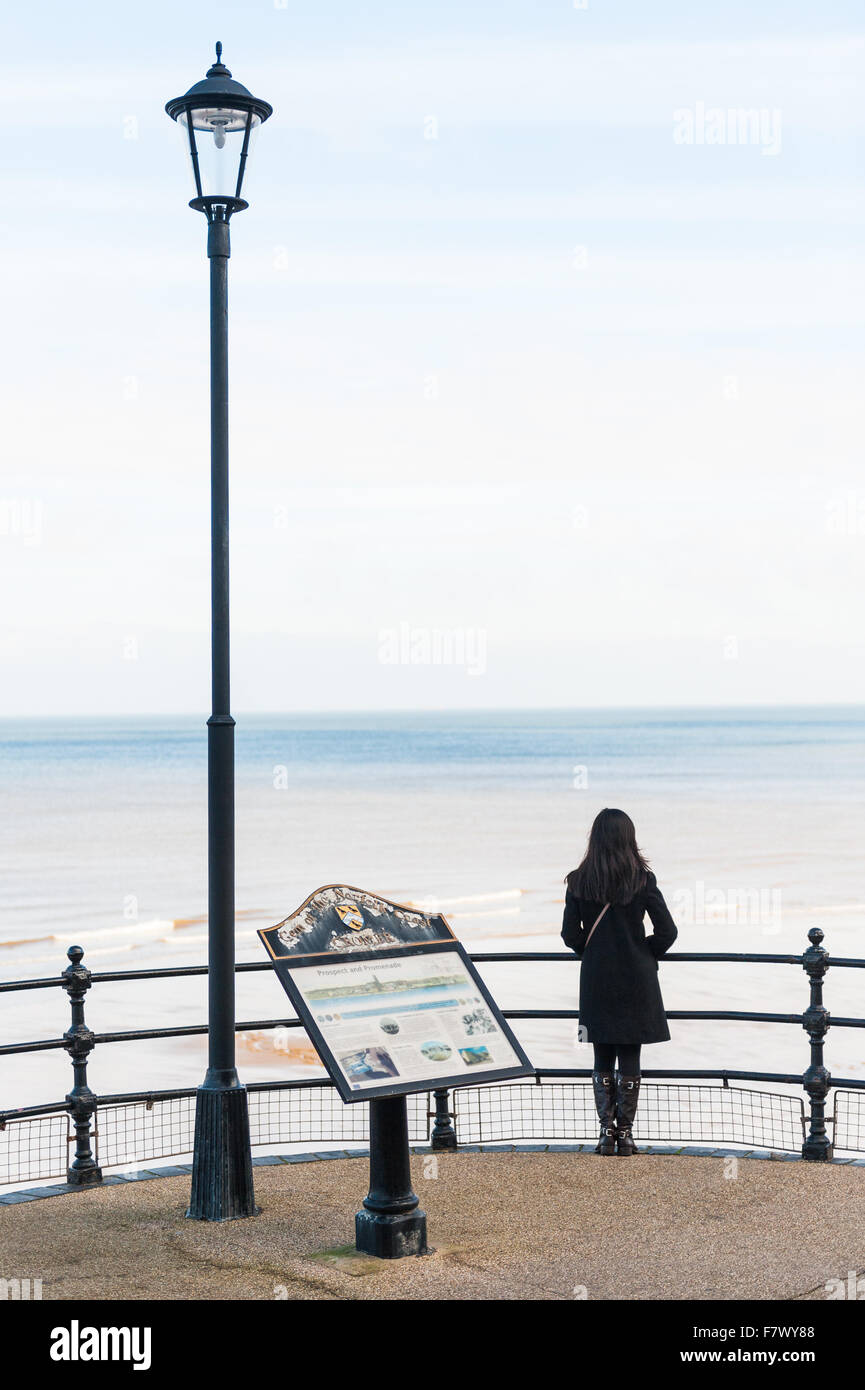 A young lady looks out to the beach and sea from the path next to Cromer Pier Norfolk, England UK Stock Photo