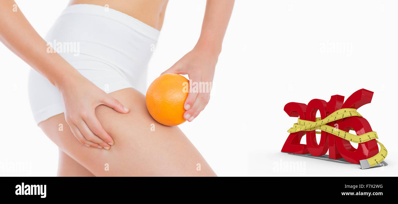 Composite image of woman squeezing fat on thigh as she holds orange Stock Photo