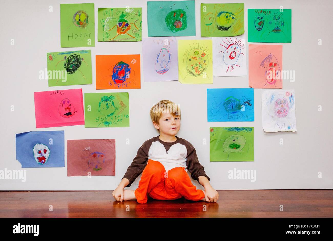 Boy sitting by wall covered in paintings and drawings Stock Photo