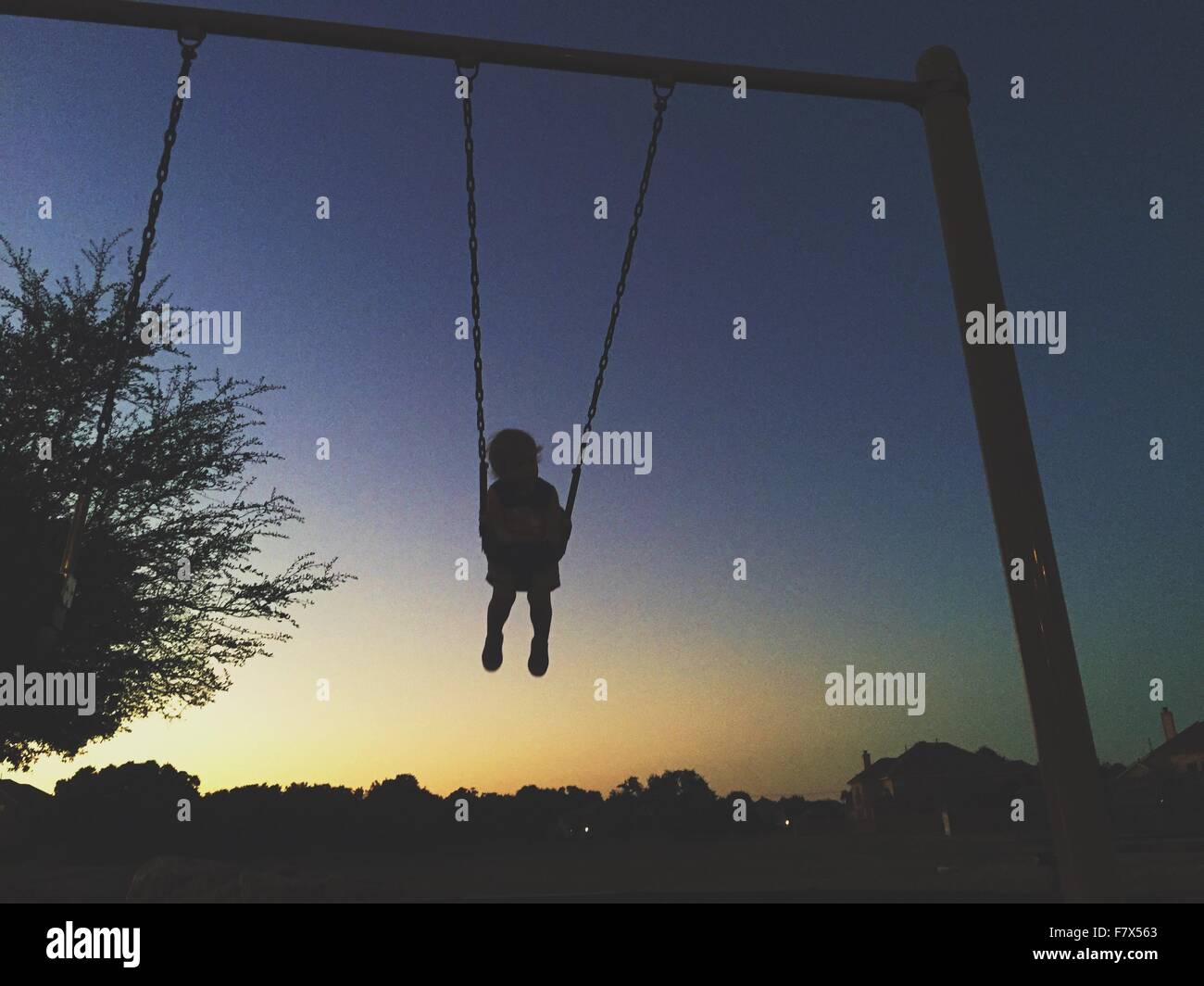 Silhouette of a toddler on swing in sunset Stock Photo