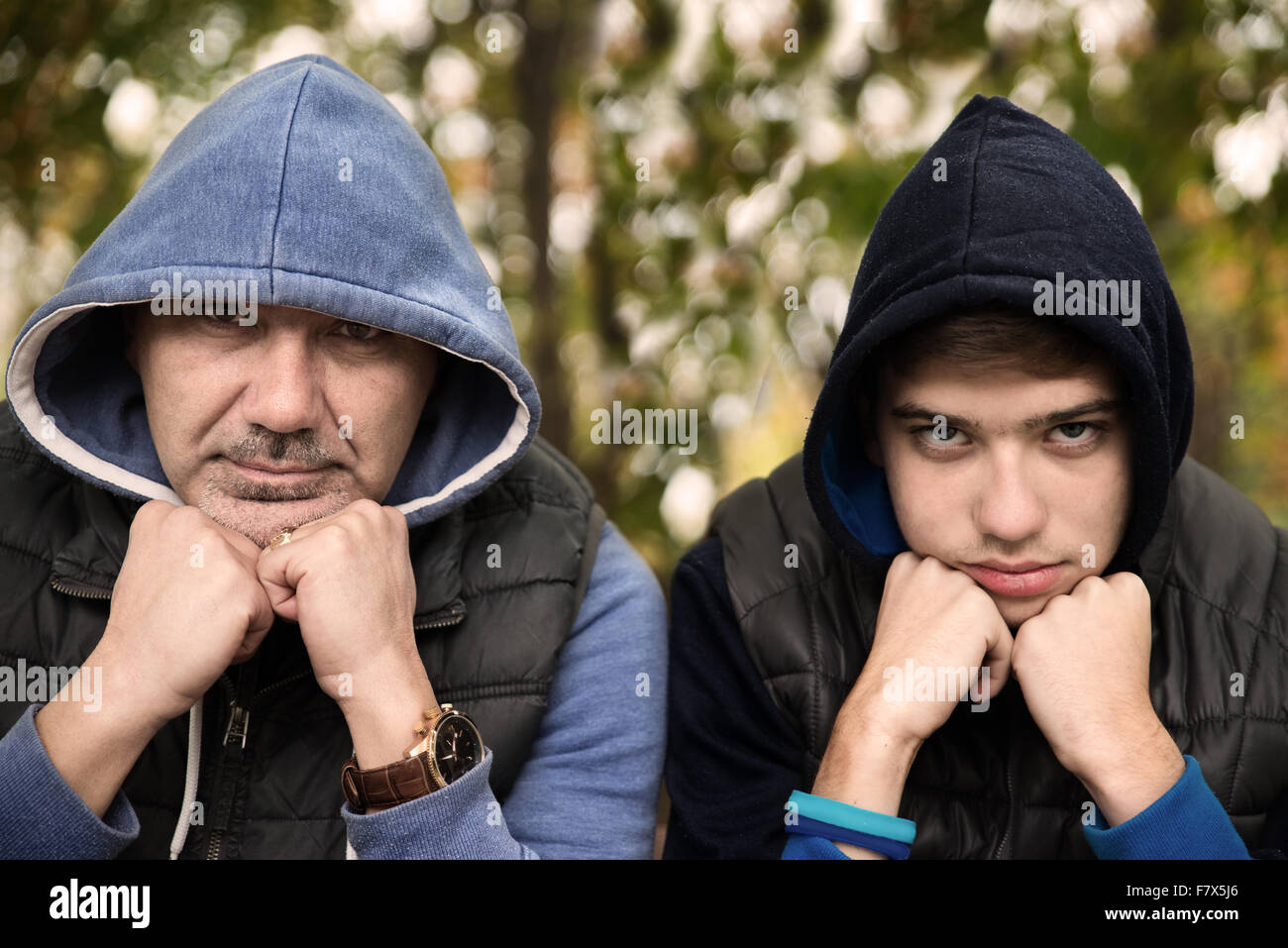 Man and teenage boy sitting in forest head leaning on their elbows Stock Photo