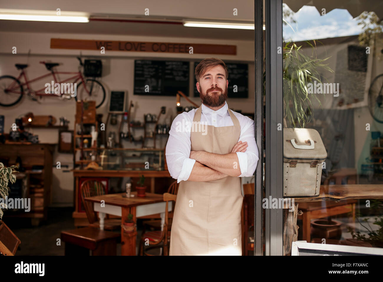 Shot of cafe owner standing proudly in the doorway of his restaurant. Young man wearing an apron standing with his arms crossed Stock Photo
