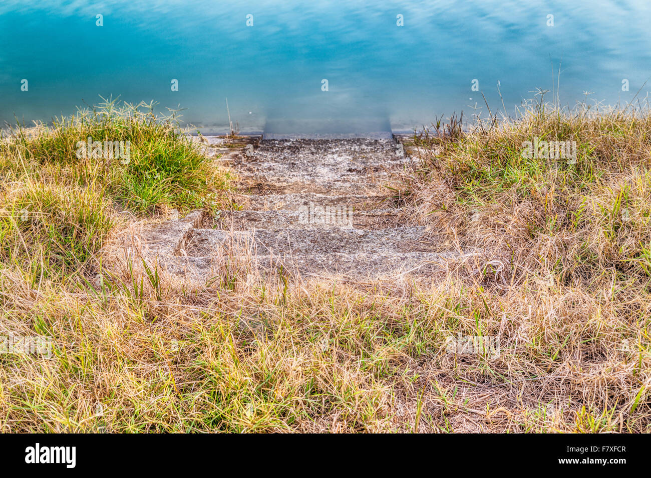 ruined stone steps leading down into the water of a canal in the country amid the scrub and weeds Stock Photo