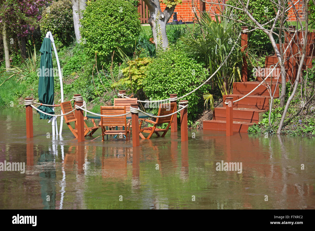 A set of wooden steps leading down to wooden chairs with a table and sunshade outside in a rear garden half covered in water Stock Photo