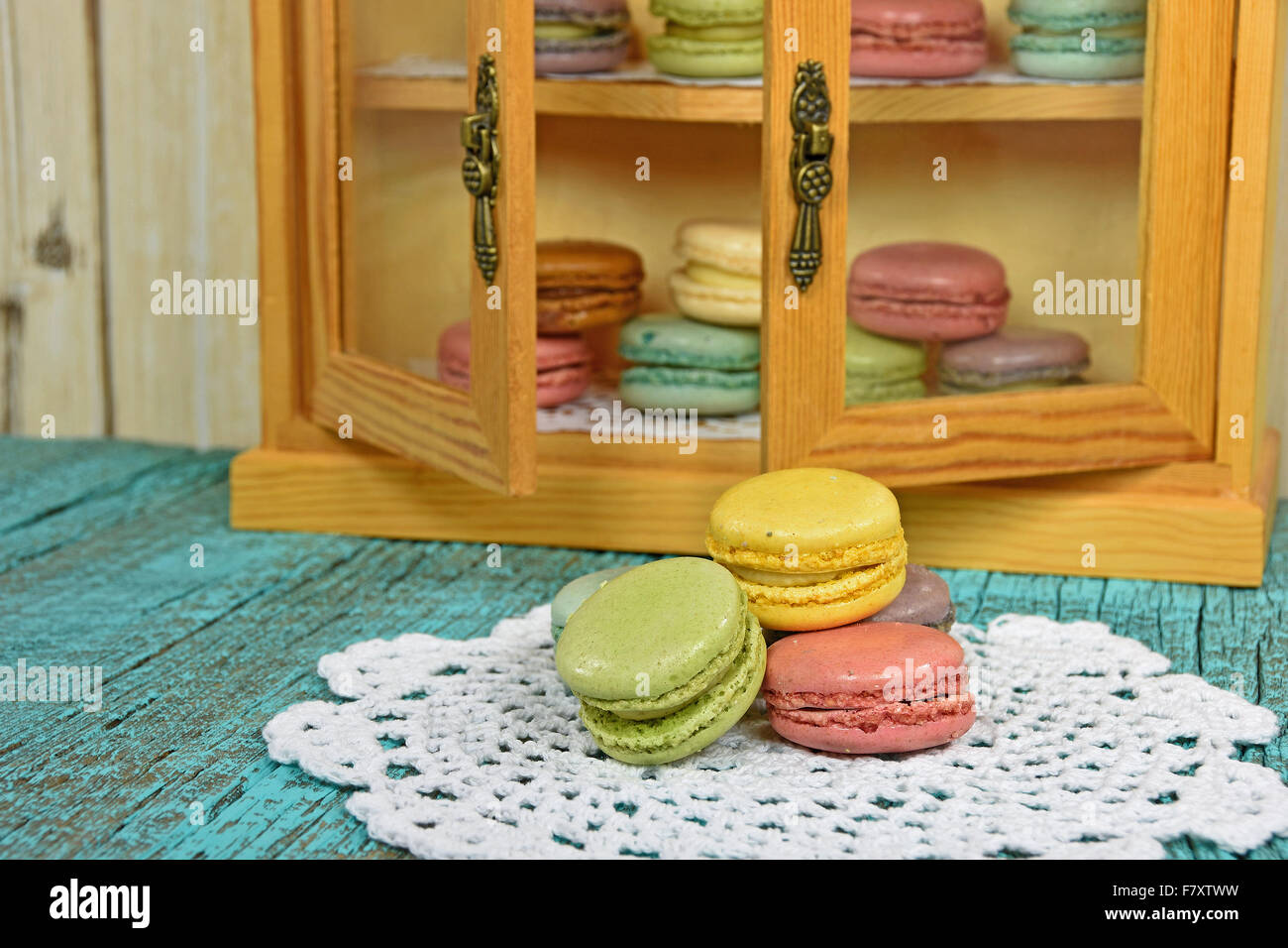 French macaroons on white lace doily with macaroons in cupboard. Stock Photo