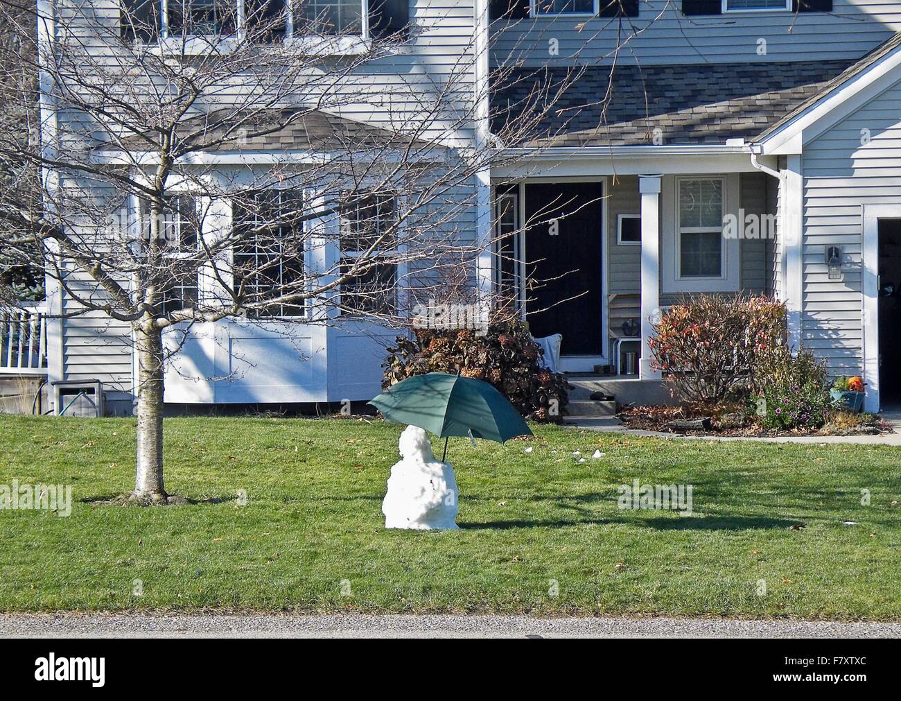 Melting snowman with green umbrella in front of suburban home. Stock Photo