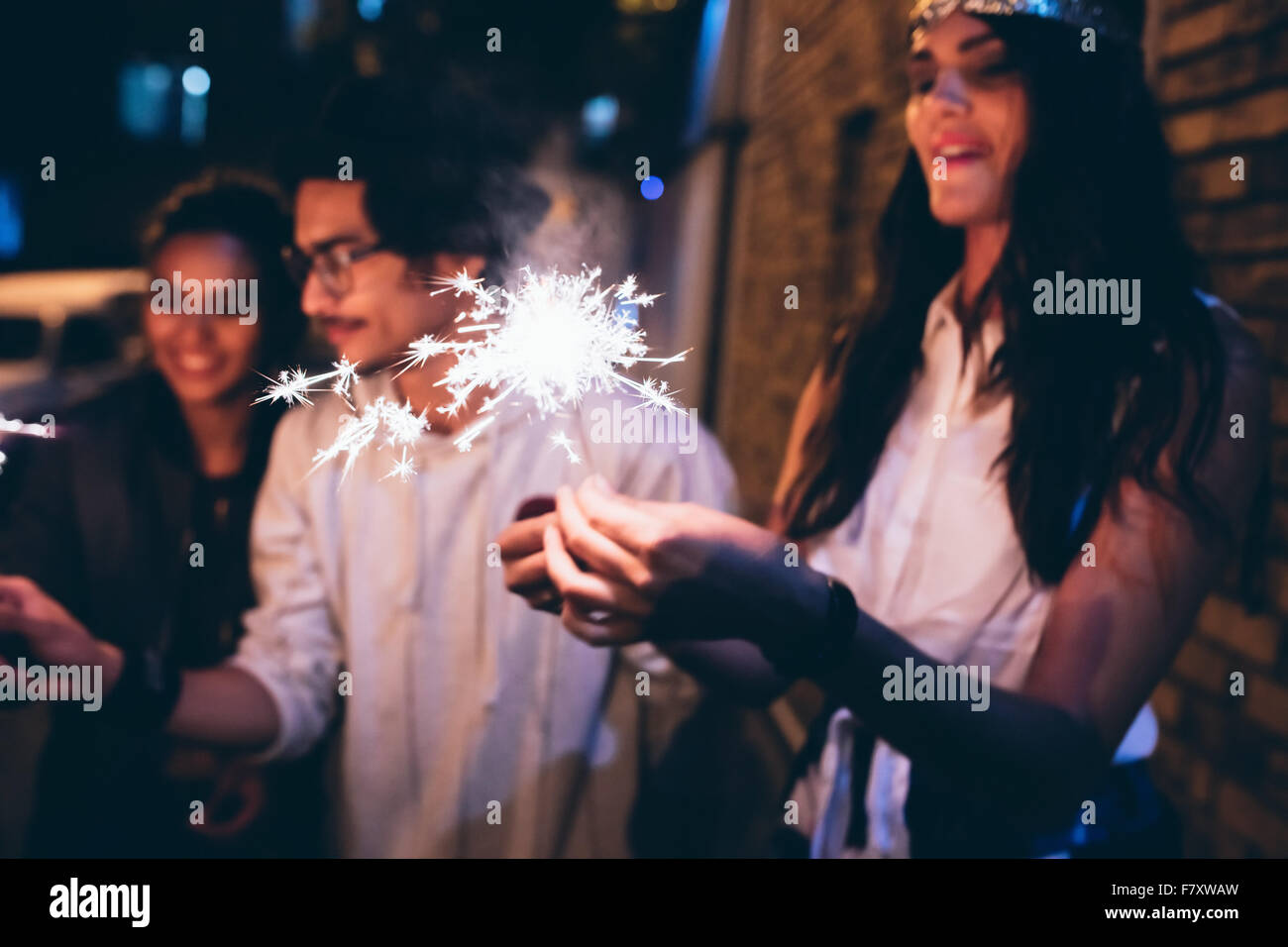 Young friends out at night, celebrating with sparklers. Men and women hanging out at night having a party. Stock Photo