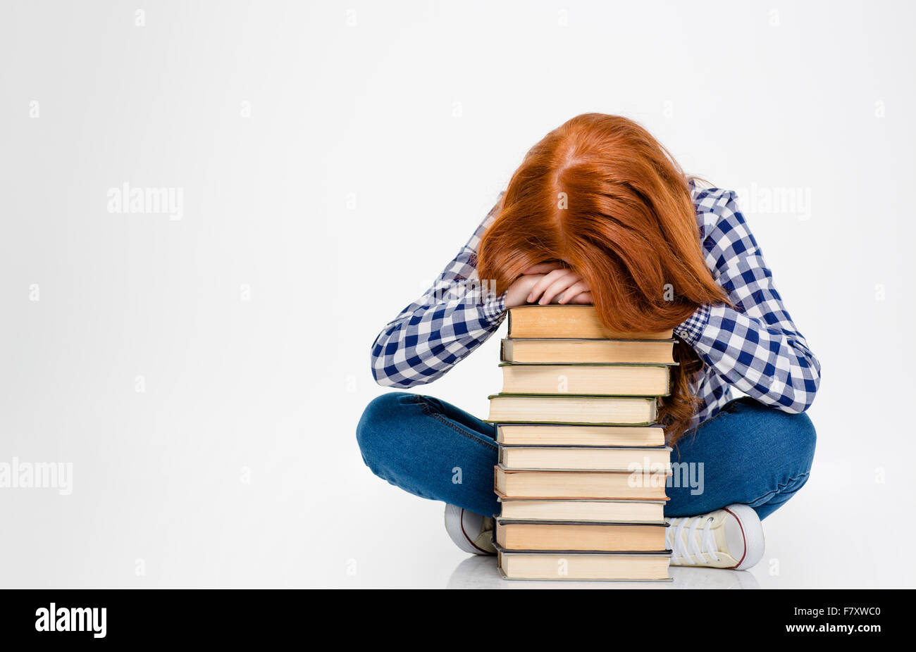 Tired exhausted young woman with red hair put head on stack of books and sleeping over white background Stock Photo