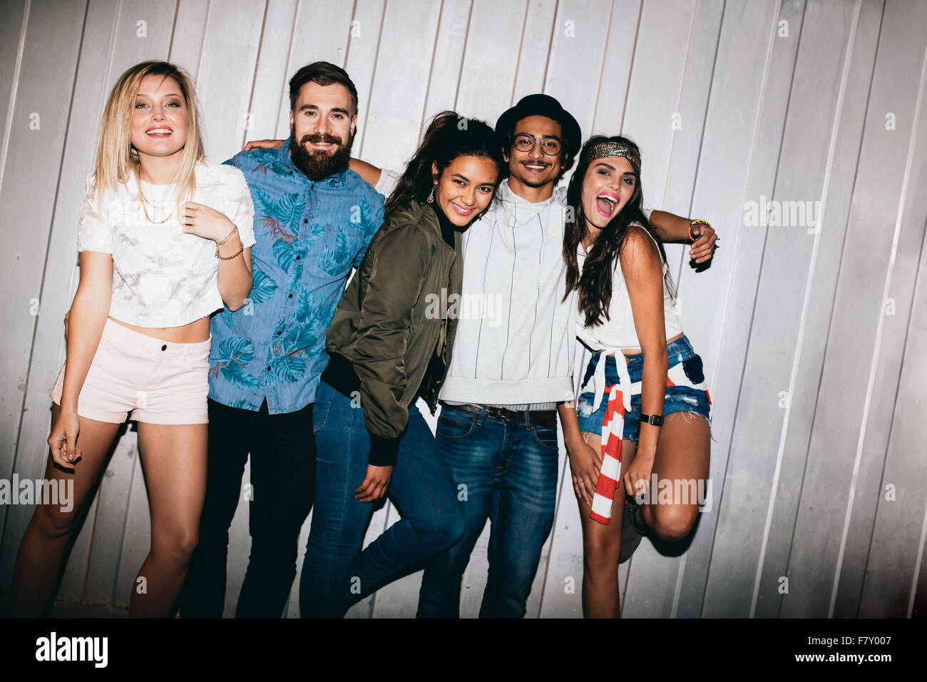 Happy young people standing together outdoors and looking at camera laughing. Young friends hanging out at night during a party. Stock Photo