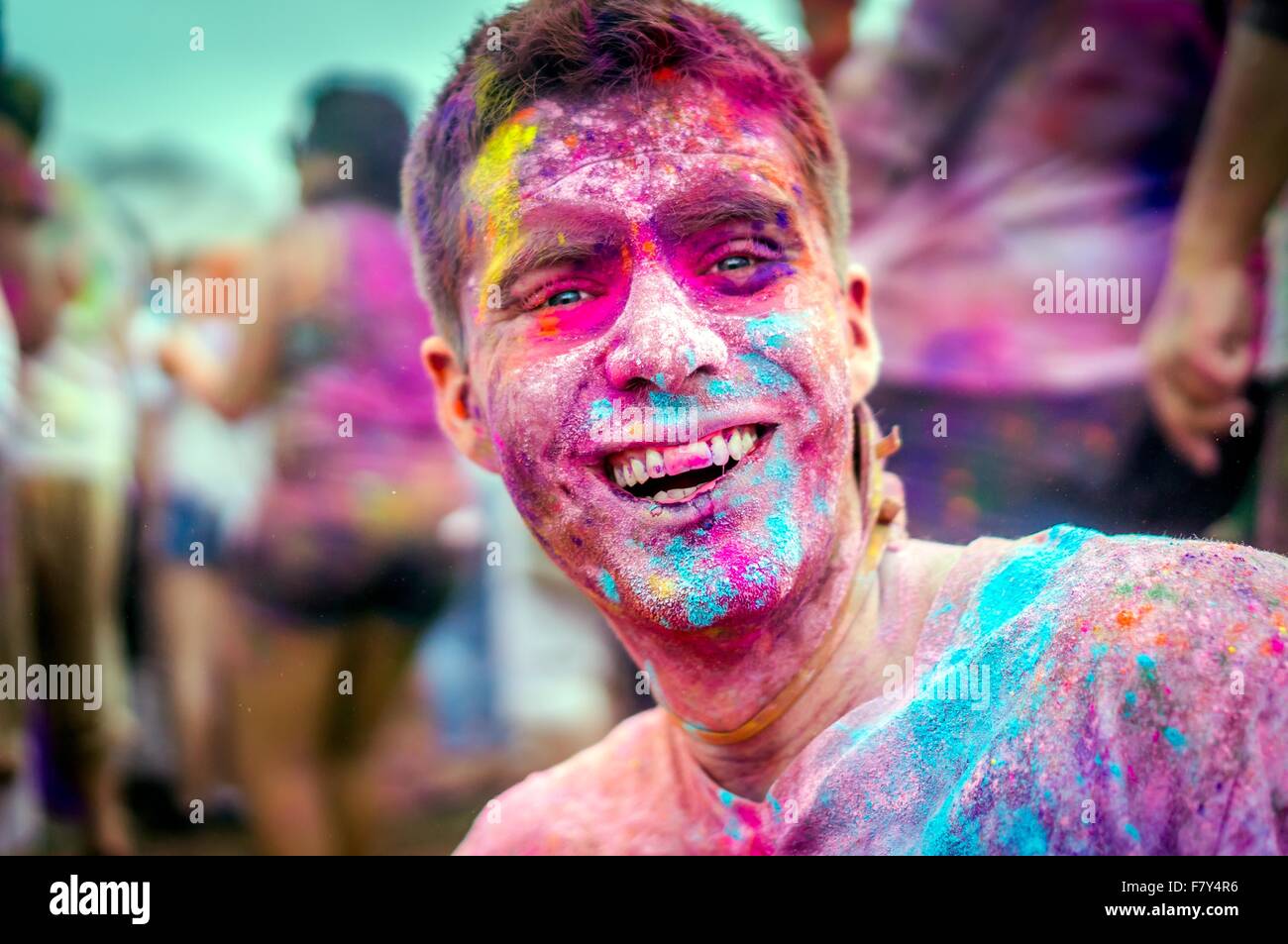 A young man covered in colored powder smiles during the Holi Festival