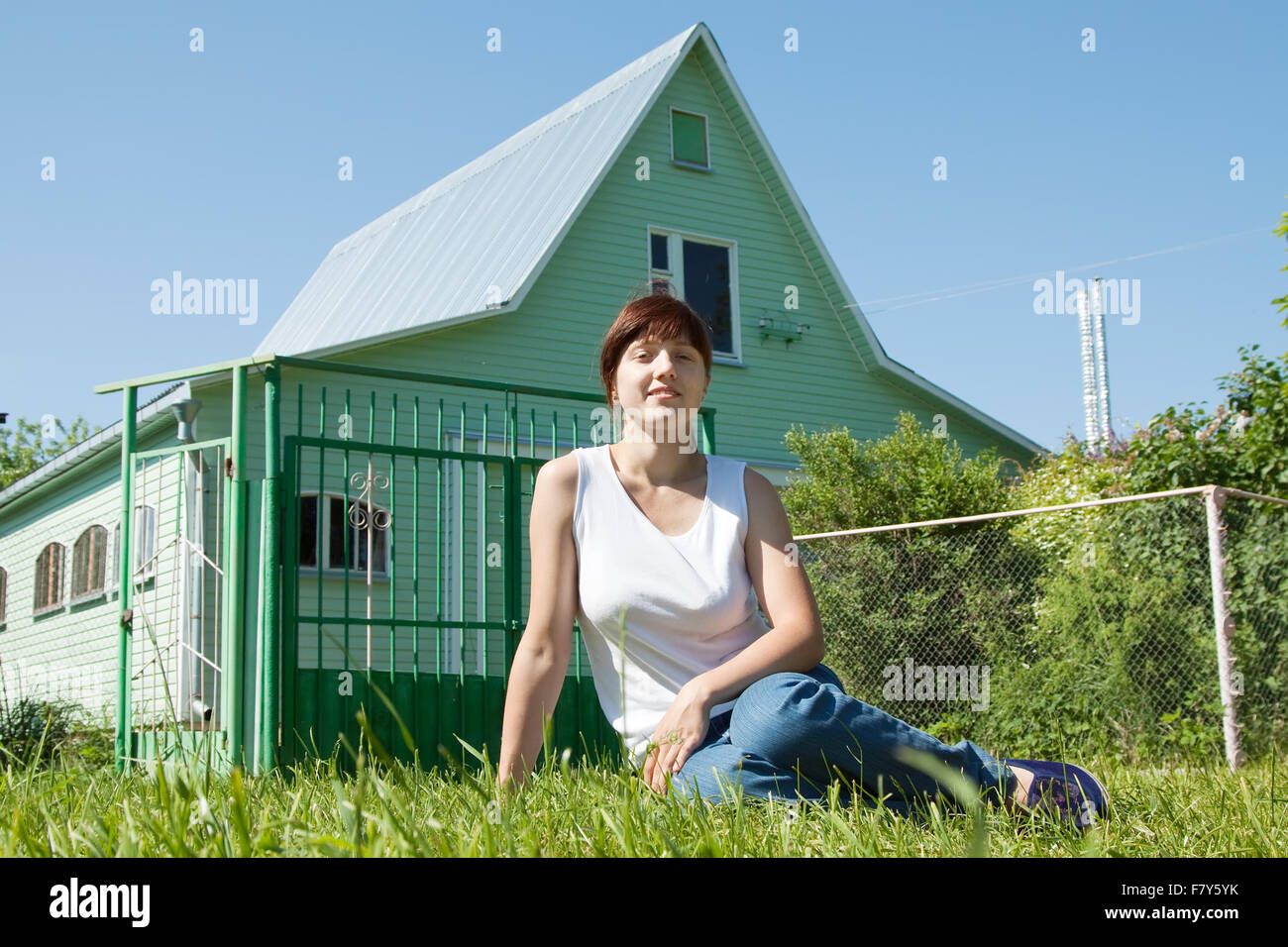 Happy young woman sitting on lawn in front of new home Stock Photo - Alamy