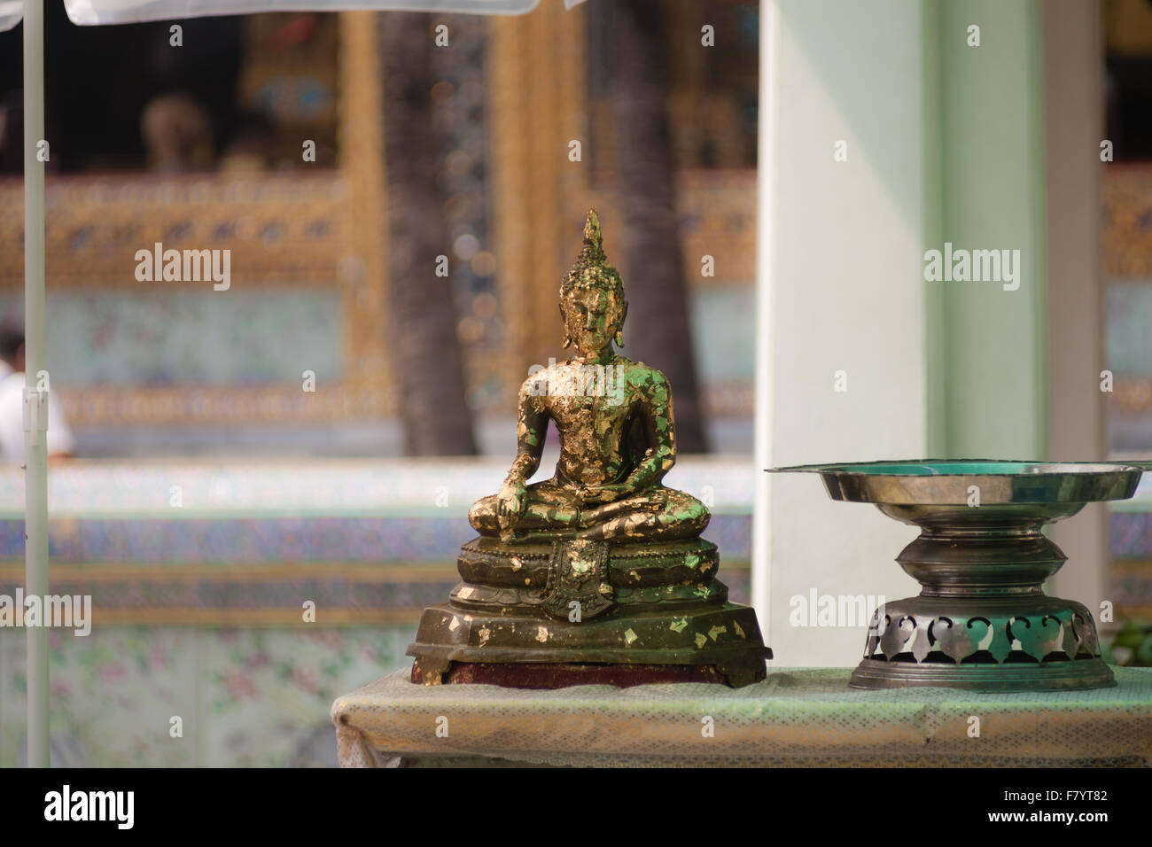 a small buddha statue with peeling gold paint outside a buddhist temple Stock Photo