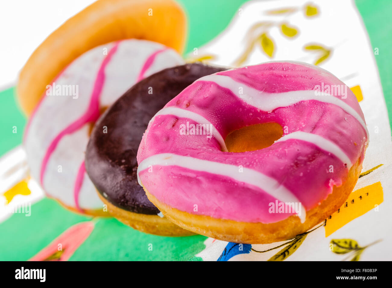 some delicious and colorful donuts on a green ornated tablecloth Stock Photo