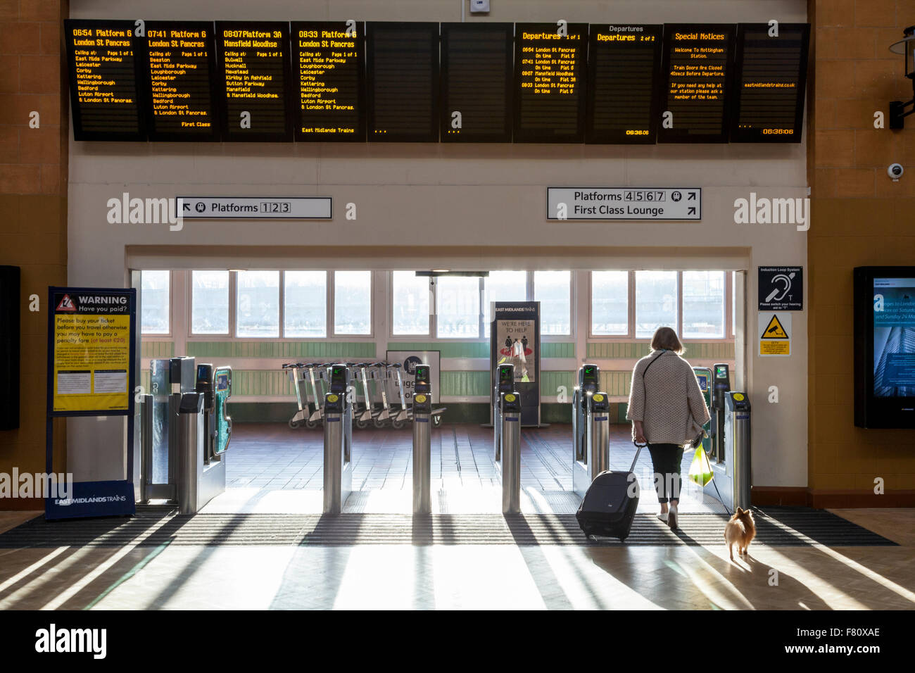 Person at a train ticket barrier and train departure board allowing access to platforms and trains at Nottingham Railway Station, England, UK Stock Photo