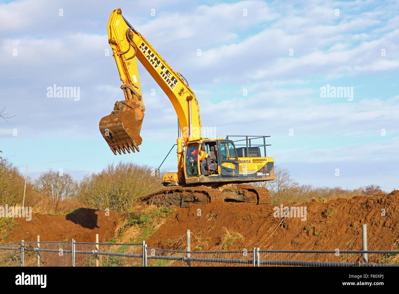 A lone digger on the top of a freshly dug earth mound, bucket and driver at the ready. Stock Photo
