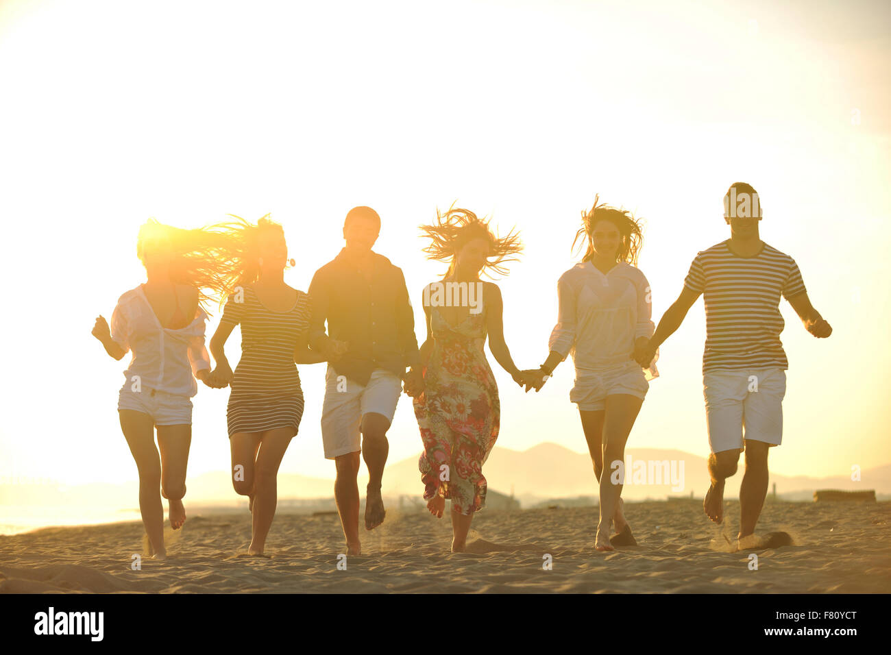 happy young people group have fun run and jump on beach beautiful sand ...