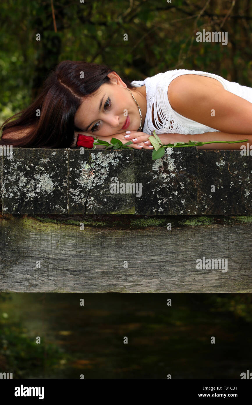 Beautiful brunette daydreaming in the park with red rose beside her. Stock Photo