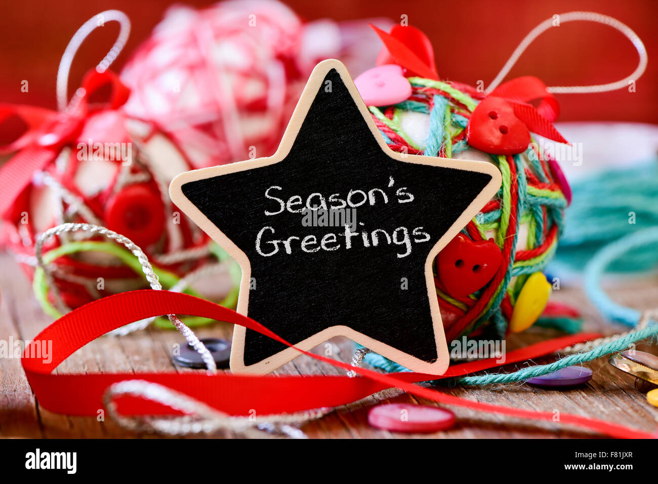 star-shaped chalkboard with the text seasons greetings and some different handmade christmas balls, made with strings, ribbons a Stock Photo